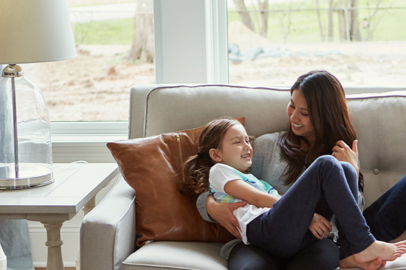 Woman and daughter snuggling on the couch in their home.